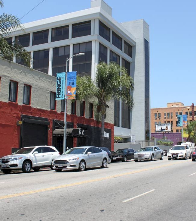 A street view of a hotel building with cars parked in front.