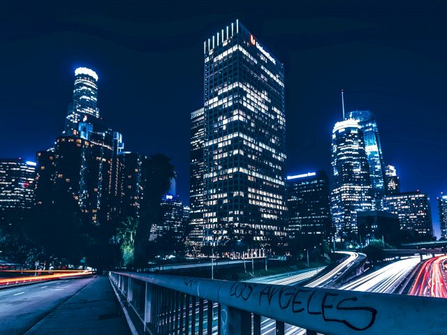 A nighttime cityscape with skyscrapers and a highway in the foreground.