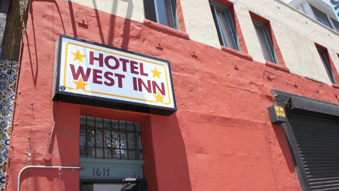 The image shows a red building with a sign that reads "Hotel West Inn" near a door marked with the number 1617, featuring stars.