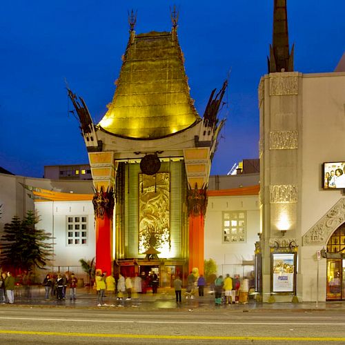 The image shows the exterior of a famous theater with ornate architecture and a golden roof, bustling with people at night.