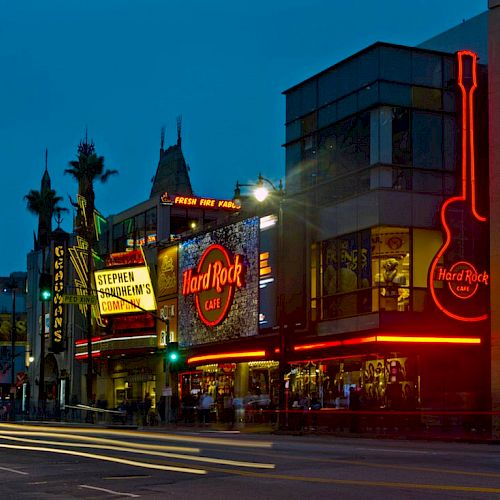 A nighttime street view with bright lights and signs, including the Hard Rock Cafe, palm trees, and busy traffic with long exposure light streaks ending the sentence.