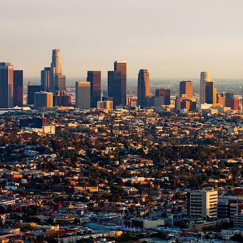 The image shows the skyline of a city with tall buildings and skyscrapers, surrounded by a densely populated urban area during daylight.