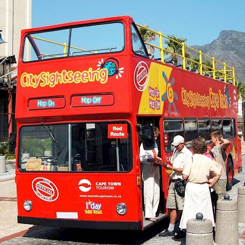 A red city sightseeing double-decker bus with tourists boarding, labeled 