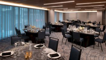 The image shows a banquet hall with round tables set for a formal event, featuring elegant table settings, chairs, and soft lighting.