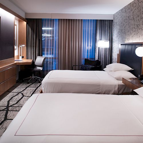 A modern hotel room with two beds, a wall-mounted TV, a work desk, and contemporary decor.
