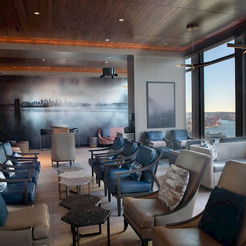 A modern lounge with leather chairs, large windows offering ocean views, and a city skyline mural on the wall.