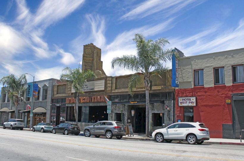 A street with parked cars, various businesses, palm trees, and a clear sky with streaked clouds ends the sentence.