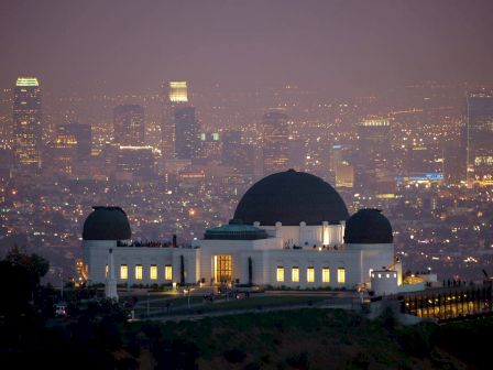 The image shows an observatory building with a domed roof, situated on a hill, overlooking a cityscape illuminated at night.